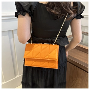 Macro shot of an orange quilted chain crossbody bag showing leather texture and gold strap