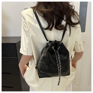 Rear view of a model wearing a black bucket backpack with silver chain drawstring