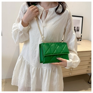 Detail of emerald green quilted bag with elegant gold chain and pearl strap decor