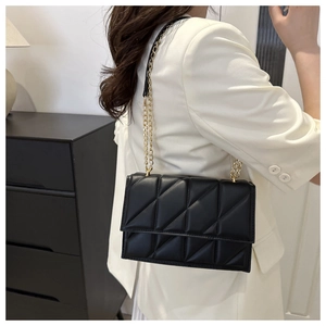 Detail of black quilted leather crossbody bag with gold chain strap on a white blazer