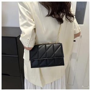 Detail of black quilted crossbody bag with gold chain strap shown on a model