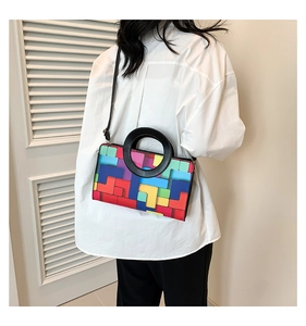 Détail du sac géométrique coloré avec grande poignée ronde noire sur chemise blanche