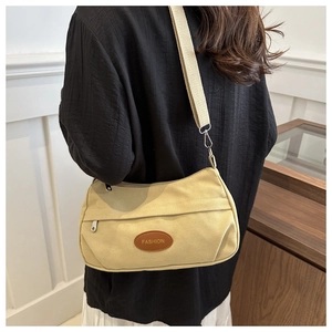 Close-up of beige canvas crossbody bag with brown leather FASHION patch and adjustable strap
