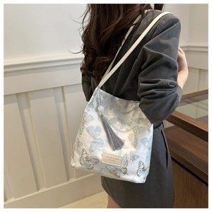 Détail du sac seau en satin blanc avec broderie de papillons et un pompon gris élégant