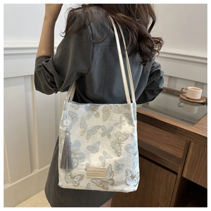 Détail d'un sac cabas blanc avec broderie papillon bleue et long gland de décoration