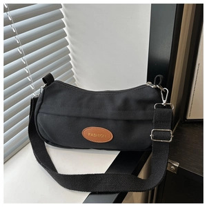 Detail of black canvas crossbody bag featuring a brown fashion leather patch and silver buckles