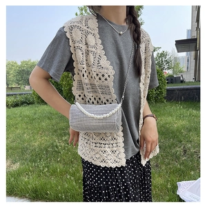Détail du sac cylindre en strass argenté avec anse en perles sur fond d'herbe verte