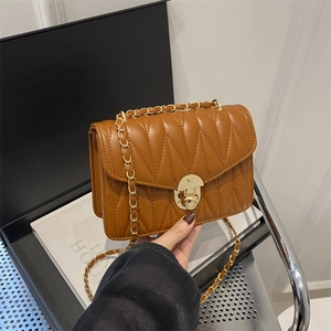 Sac bandoulière marron matelassé avec surpiqûres en V et chaîne dorée tenu à la main