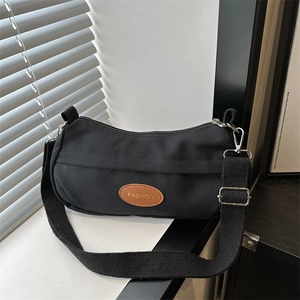 Minimalist black canvas shoulder bag with adjustable strap and leather fashion label