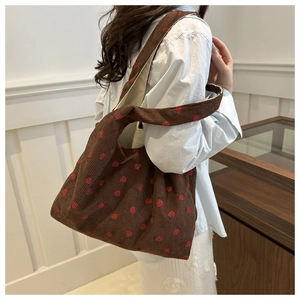 Sac fourre-tout en velours côtelé marron avec broderie fraise porté par un mannequin