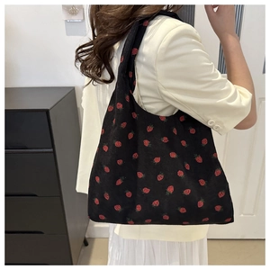 Détail du motif fraise sur un sac cabas en velours côtelé noir porté à l'épaule
