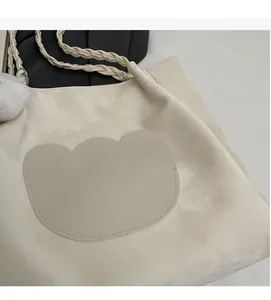 Gros plan du sac cabas beige en daim avec poignées tressées et pompon en peluche
