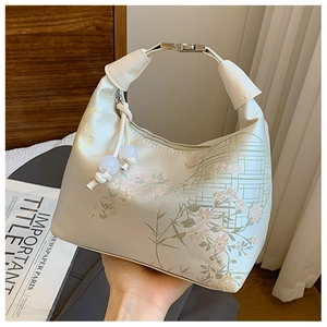 Detail of cream shoulder bag with floral embroidery and decorative beaded zipper pull