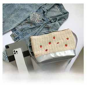 Détail du sac seau en paille tressée avec broderie fraise et base métallisée