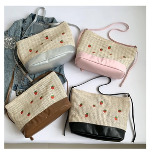 Détail de broderie fraise sur sac seau en paille avec finitions en similicuir chic