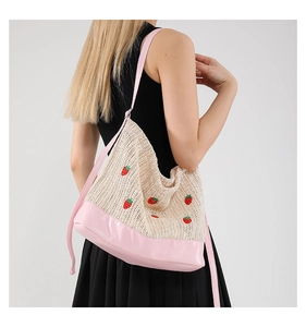 Détail de broderie fraise sur sac hobo en paille tressée avec bandoulière rose