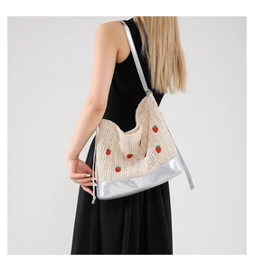 Détail de broderie fraise sur sac seau en paille avec garniture en cuir argenté