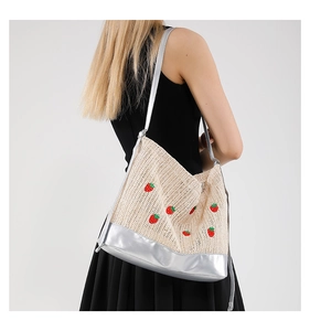 Détail du sac seau en paille avec motif fraise et bandoulière argentée métallisée