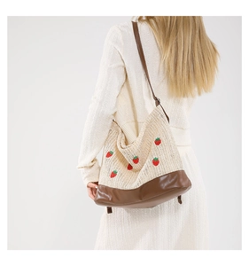 Détail du sac seau en paille avec broderie de fraises et garniture en cuir marron