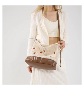 Gros plan détaillé de la broderie fraise sur le sac seau en paille beige avec bandoulière cuir