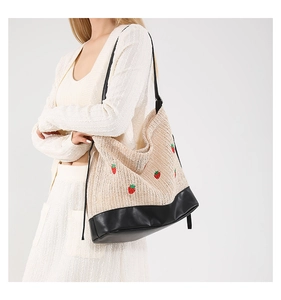 Détail du sac seau en paille tressée avec broderie fraise rouge et base en cuir PU noir