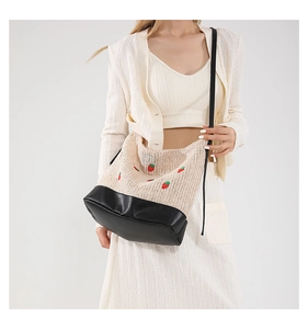 Détail du sac seau tressé avec broderie fraise et base en cuir noir porté par un mannequin
