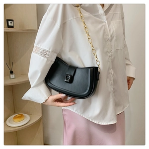 Detail of a black semi-circle saddle bag with a chunky gold chain strap worn by a person