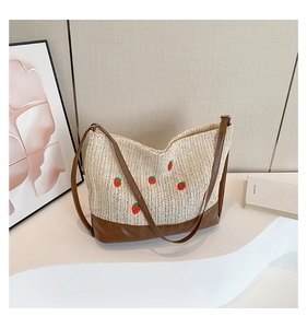 Détail du sac seau en paille tressée avec broderie fraise et bandoulière en cuir marron