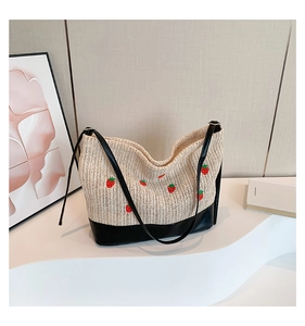 Détail d'un sac cabas en paille tissée avec broderie fraise et bandoulière en cuir noir