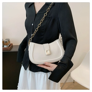 Detail of a white half-moon underarm bag with a gold chain strap and square buckle