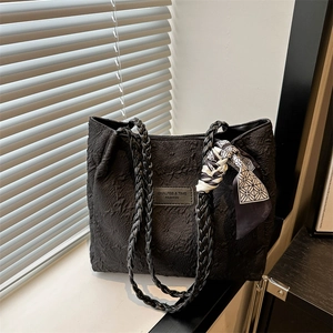 Large black textured tote bag with braided handles and decorative silk scarf on a windowsill