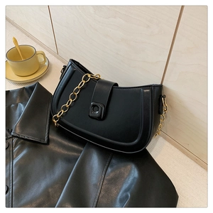 Close-up of black PU leather half-moon bag with gold chain strap on leather jacket