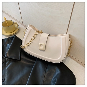 Close-up of cream saddle bag with gold chain strap on black leather background