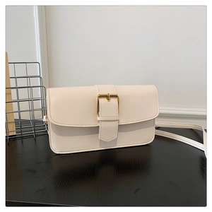Détail d'un petit sac carré blanc cassé avec une boucle rectangulaire dorée en métal