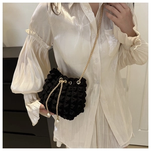 Detail of black bubble texture bucket bag with gold chain and elegant pearl drawstrings