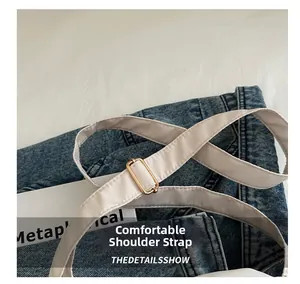 Detail of adjustable off-white fabric strap with gold metal buckle on denim background