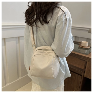 Detail of a beige nylon crossbody bag with adjustable strap and side orange label