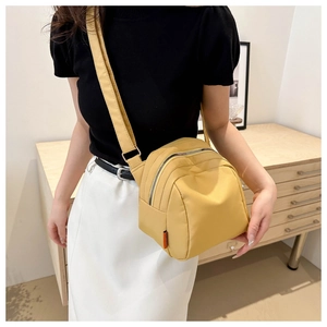 Detail of a bright yellow nylon crossbody bag with adjustable strap and side orange label