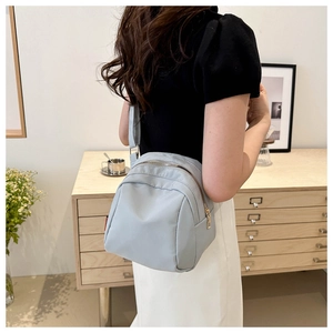 Close-up of a light blue-grey nylon shoulder bag with silver zipper and red side label detail