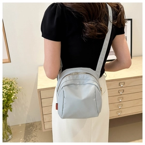 Detail showing light blue nylon mini crossbody bag with smooth texture and metal zippers