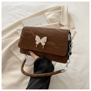 Detail of a brown pleated shoulder bag with a marble-textured bow accent and silver chain