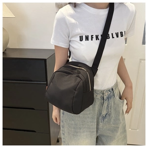 Close-up of a compact black nylon crossbody bag worn by a model in a modern interior