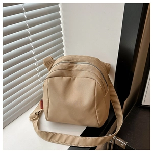 Detail view of beige nylon shell bag with dual silver zippers and red fashion tag