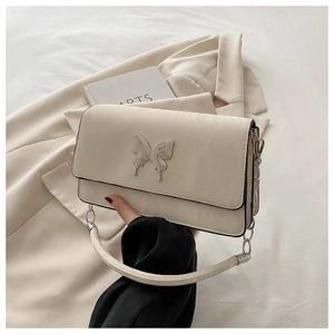 Detail of cream-white leather shoulder bag with silver butterfly metal ornament and chain