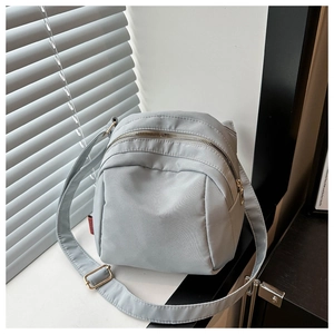 Close-up of light grey nylon crossbody bag featuring smooth zipper and red side label