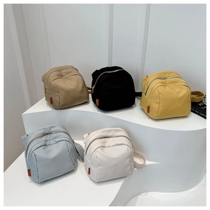 Five nylon crossbody bags in different colors displayed on white geometric stands