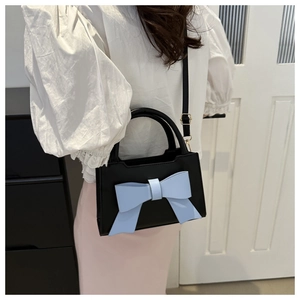 Detail of black PU leather crossbody bag with a large light blue decorative bow