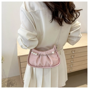 Detail of pink pleated crossbody bag with pearl chain and heart charms on a model