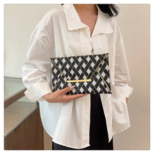 Détail de la pochette enveloppe tressée noire et blanche avec bordure en métal doré élégante
