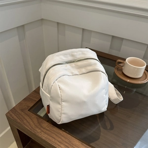 Lightweight white nylon shell bag with orange tag on wooden table in casual setting